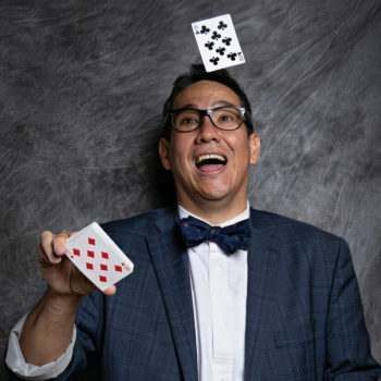 A man in a suit and bow tie is throwing playing cards in the air.