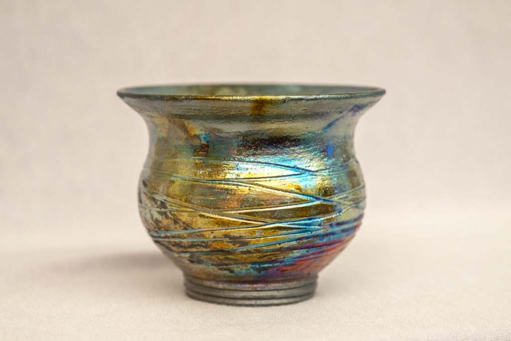 A small colorful vase is sitting on a white surface.