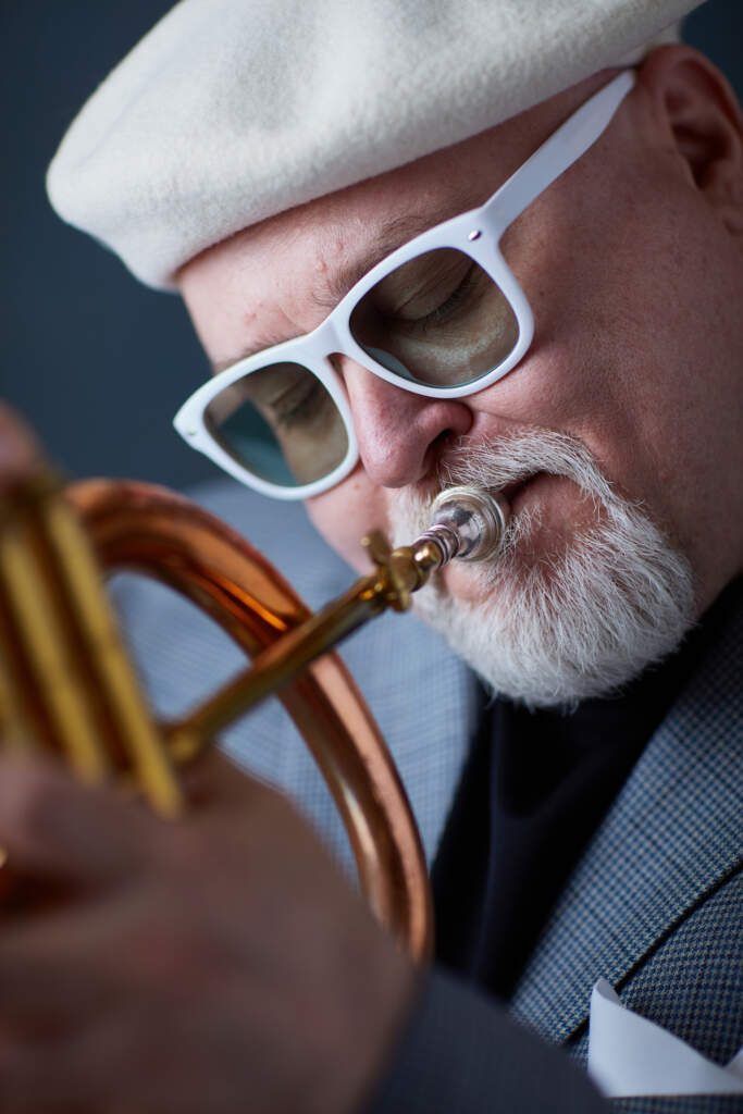 A man wearing a white hat and sunglasses is playing a trumpet