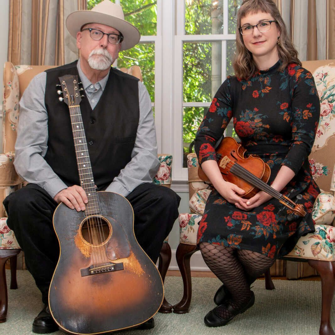 A man holding a guitar and a woman holding a violin