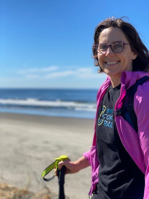 A woman in a pink jacket is standing on a beach holding a leash.