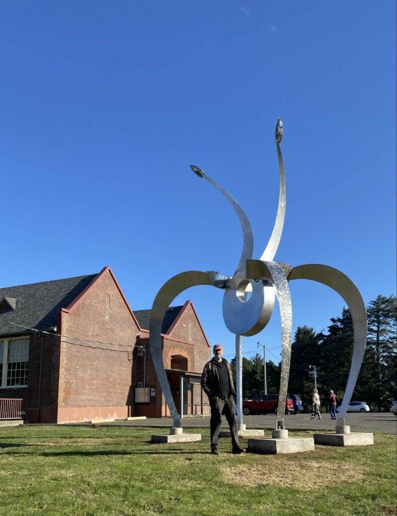 A man is standing in front of a large sculpture in a park.