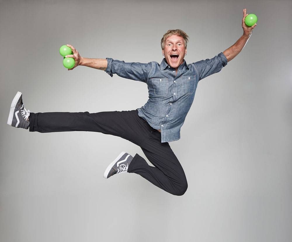 A man is jumping in the air while holding two green balls in his hands.