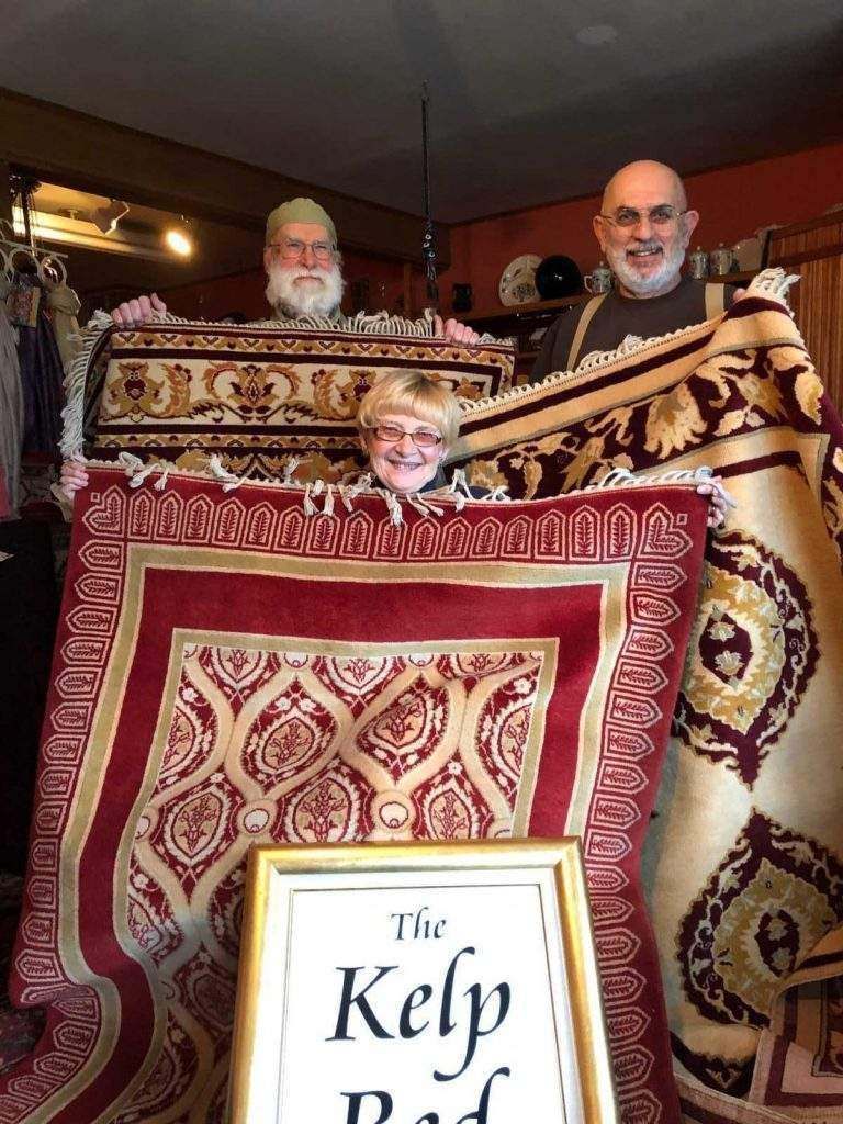 Three men are holding a large rug and a sign that says the kelp pad.