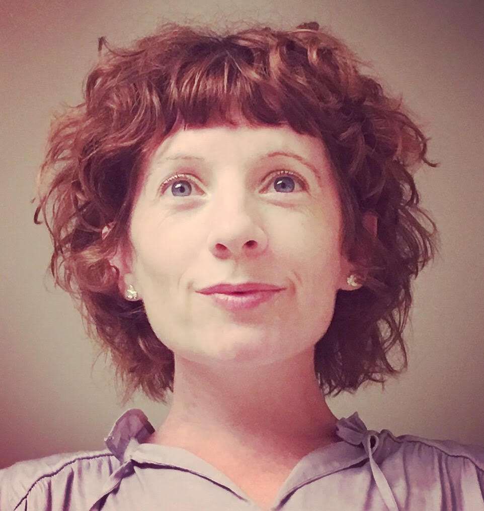 A woman with curly hair is smiling for the camera