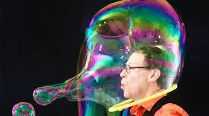 A man is blowing soap bubbles in front of a giant soap bubble.
