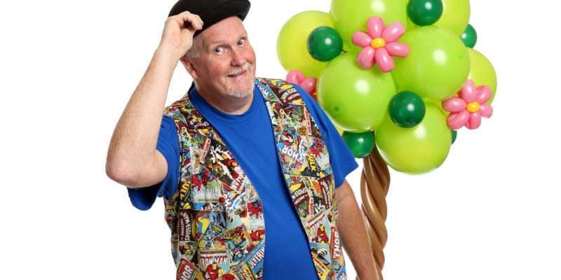 A man is holding a bunch of green balloons with flowers on them.