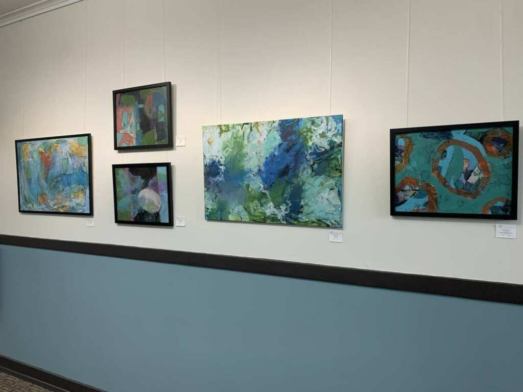 A row of paintings hanging on a wall in a hallway.