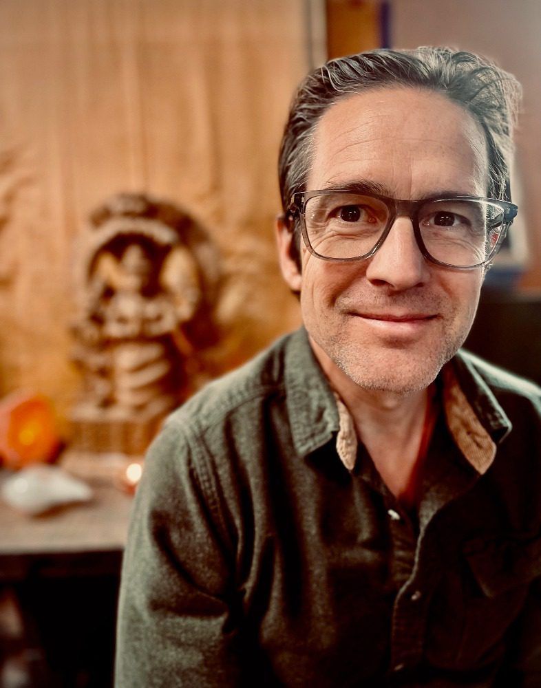 A man wearing glasses and a green shirt is sitting in front of a statue.