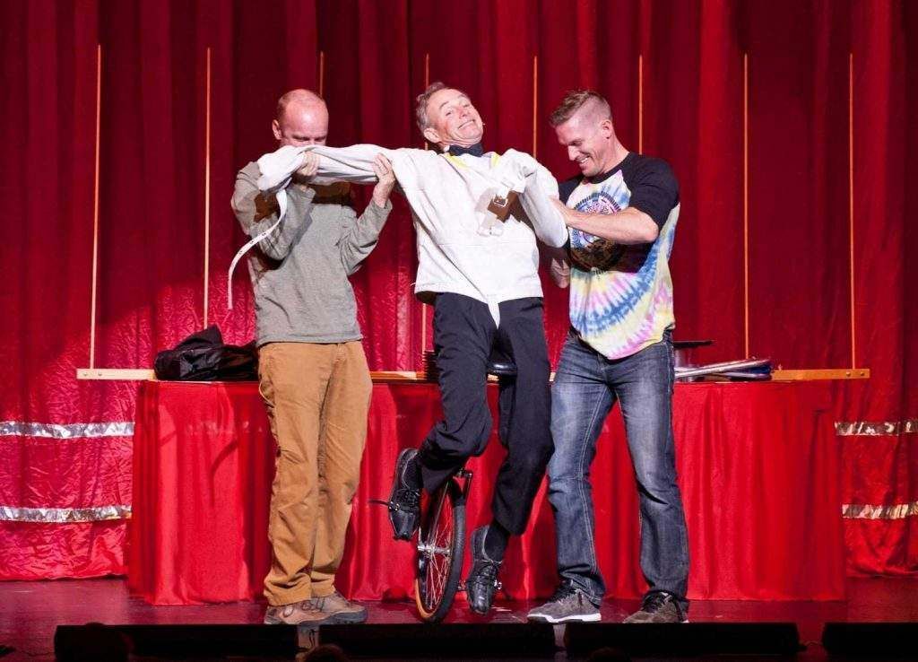 Three men are standing next to each other on a stage in front of a red curtain.