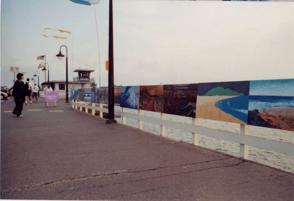 A person walking down a sidewalk next to a wall with paintings on it