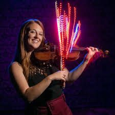 A woman is playing a violin with fireworks behind her.