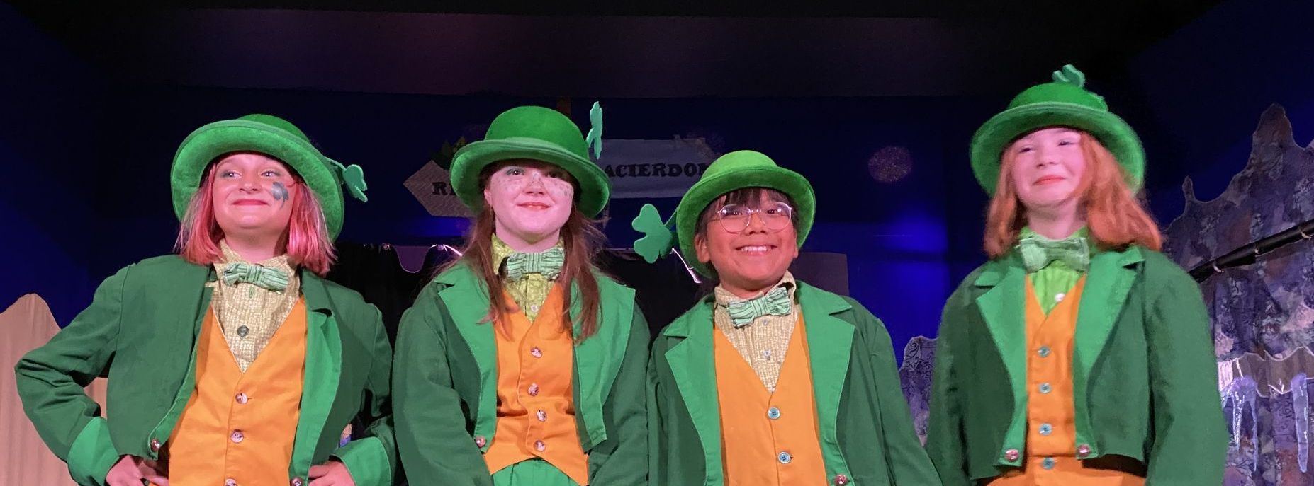 A group of young girls dressed in green and orange costumes are standing next to each other on a stage.
