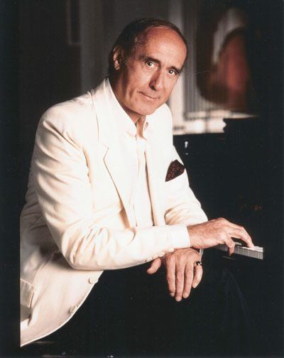 A man in a white suit is sitting at a piano