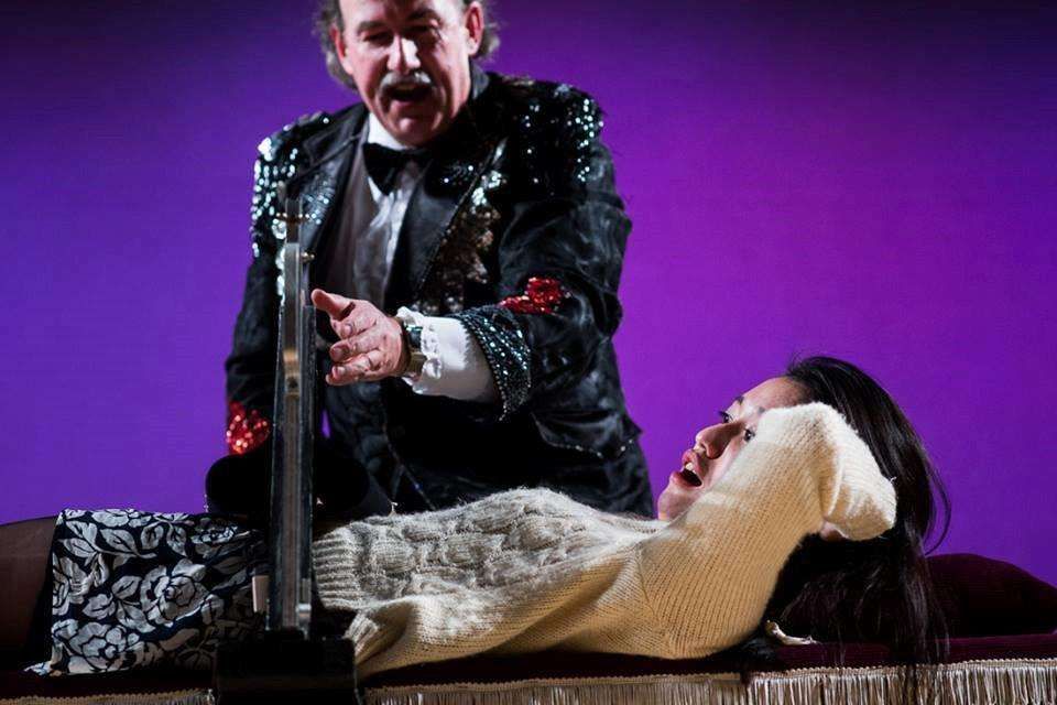 A man in a tuxedo is performing a trick on a woman laying on a table.