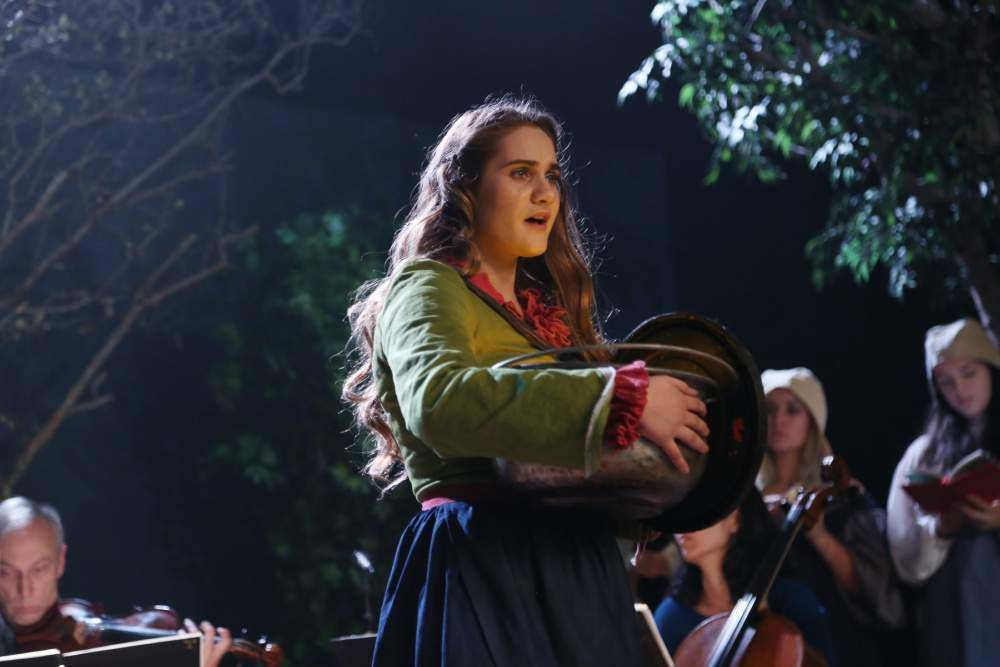 A woman is singing into a microphone in front of an orchestra.