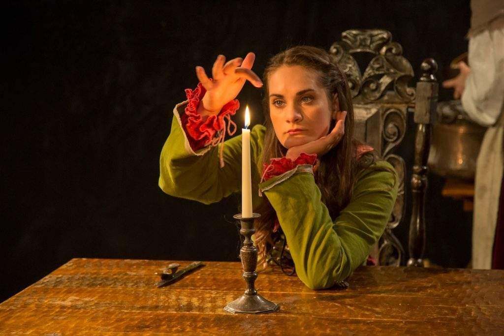 A woman is sitting at a table holding a lit candle.