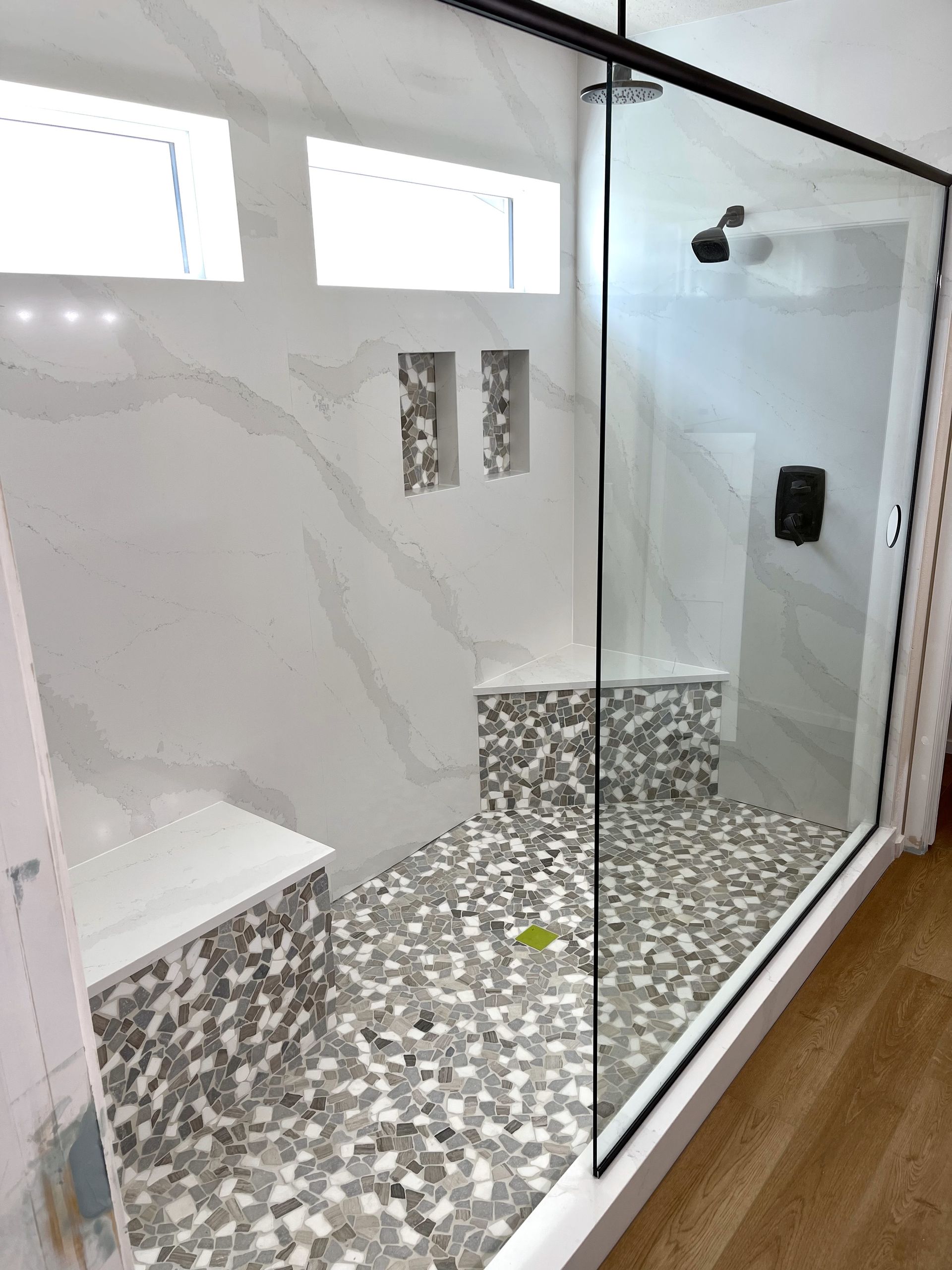 Modern shower with glass door, marble tile, pebble floor, built-in seat and niches.