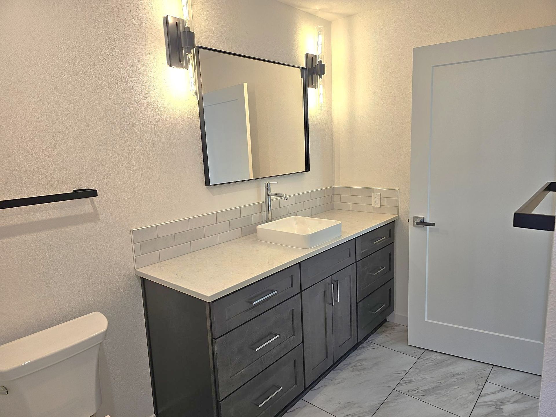 Modern bathroom with gray vanity, white countertop, rectangular mirror, and white door.