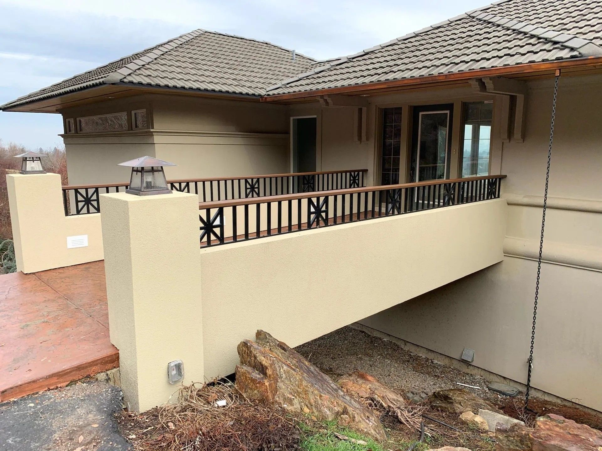 Tan stucco house with a wooden balcony, brown roof, and rocks in the foreground.
