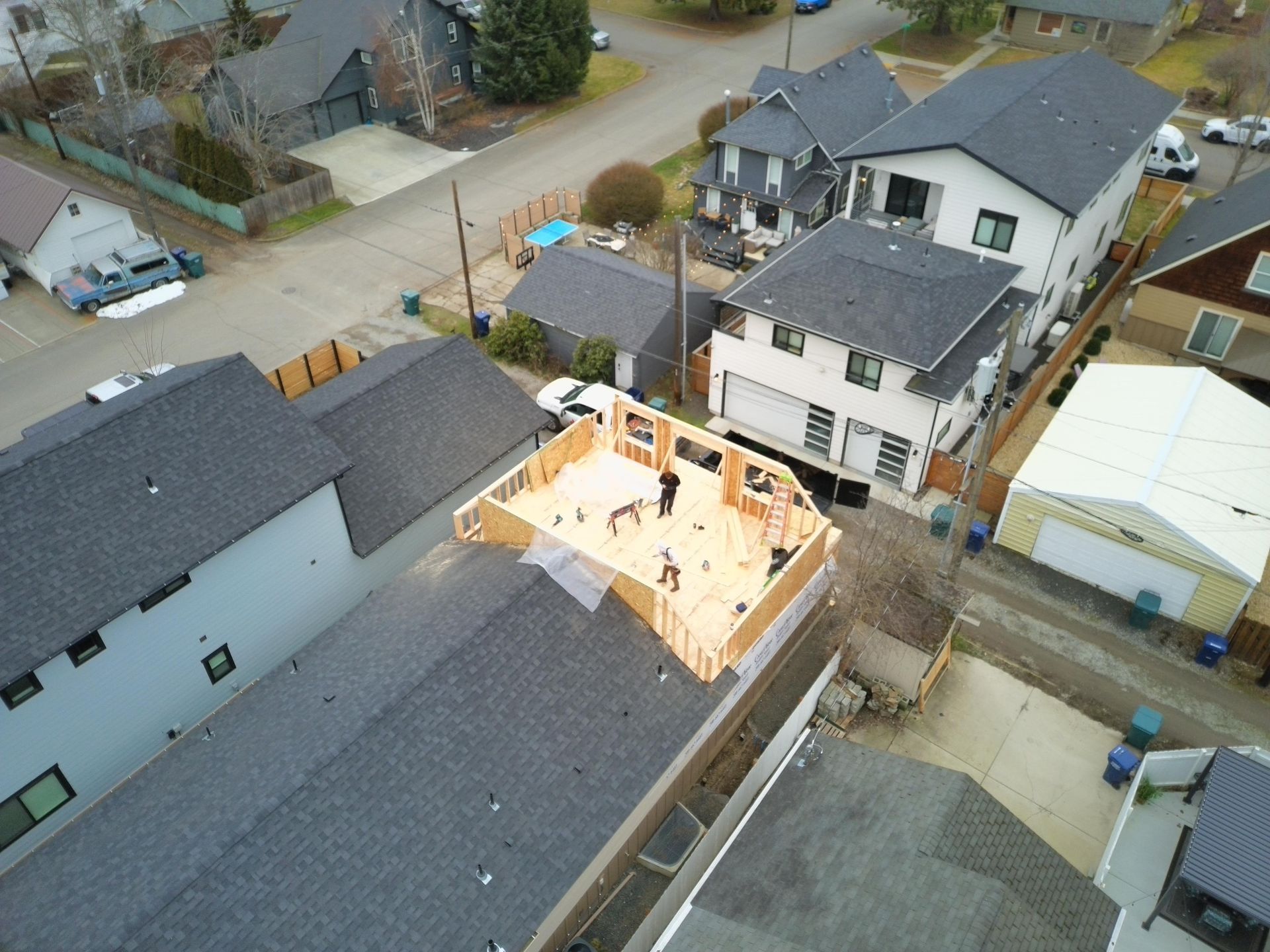 Aerial view of house construction; wooden frame on a gray roof, workers present.