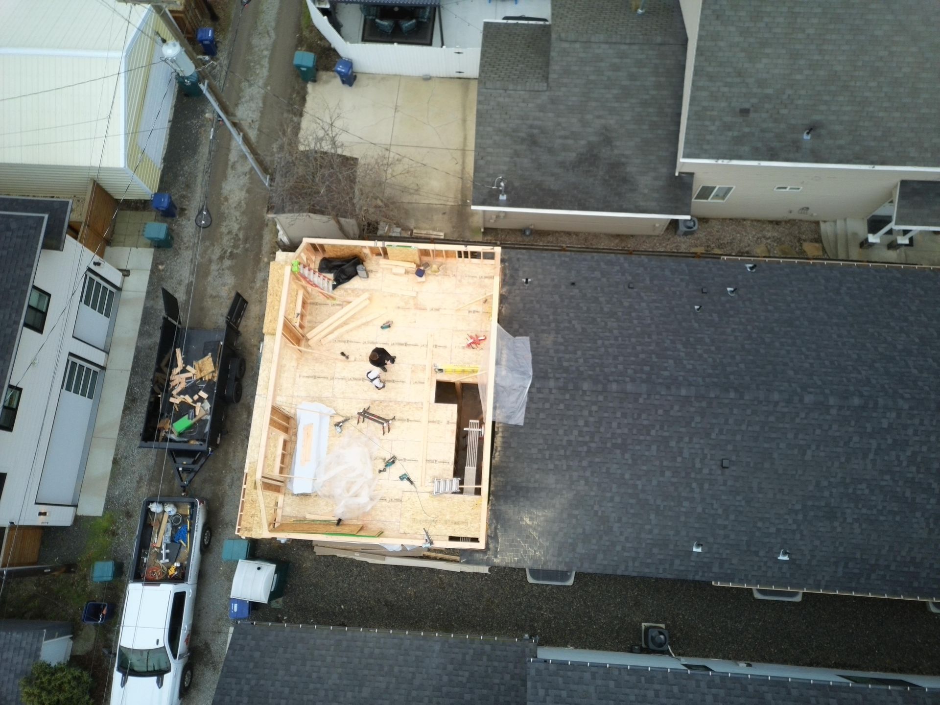 Aerial view of a building under construction, wooden frame on a roof, surrounded by other buildings and vehicles.