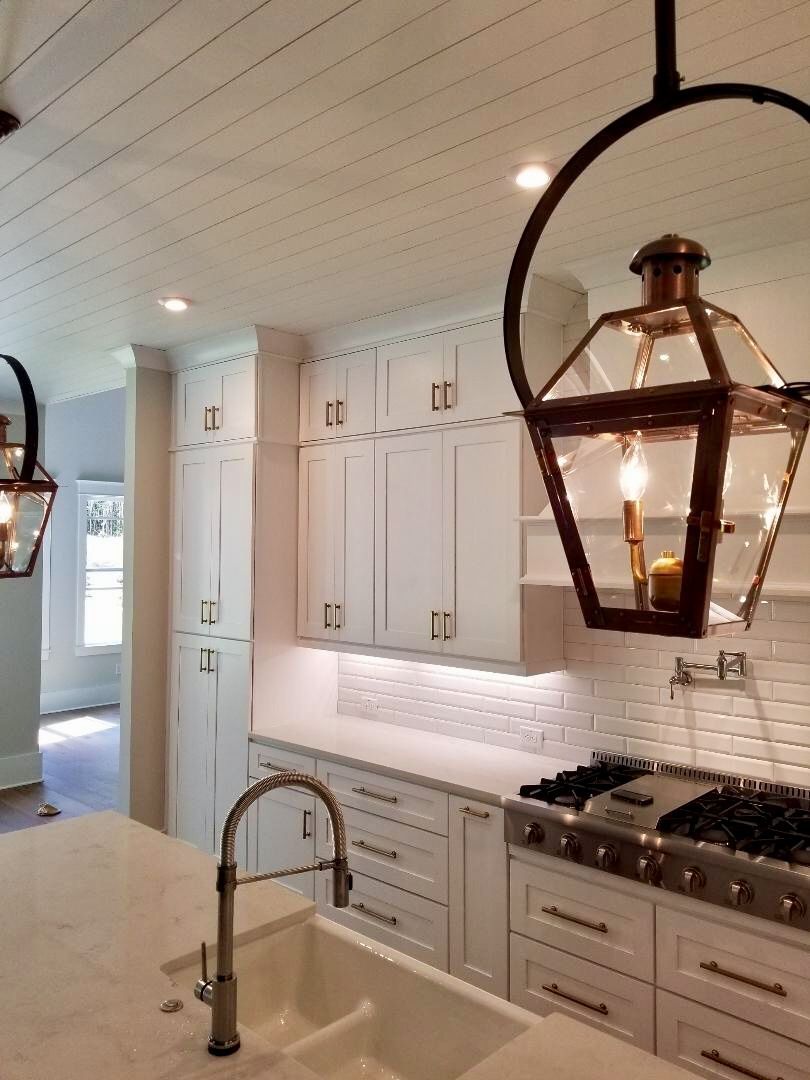 White kitchen with cabinets, sink, stove, and hanging lantern lights.