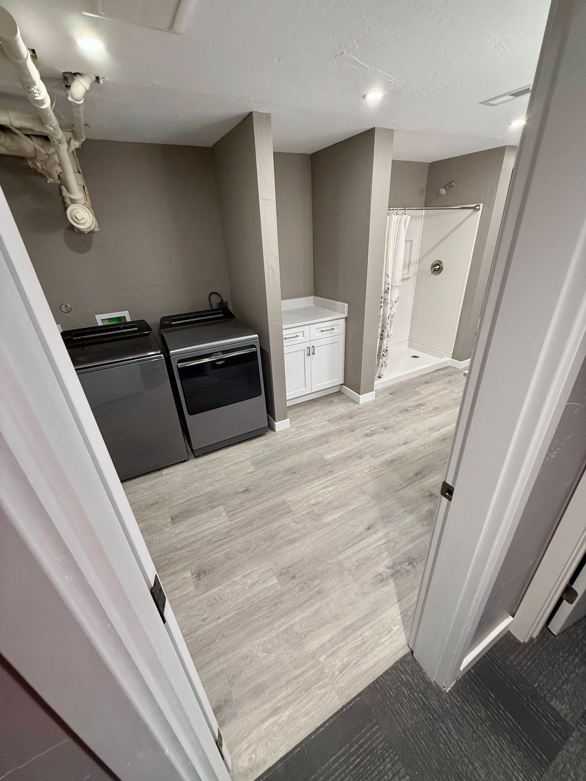 Laundry room with washer, dryer, sink, shower, and gray flooring.