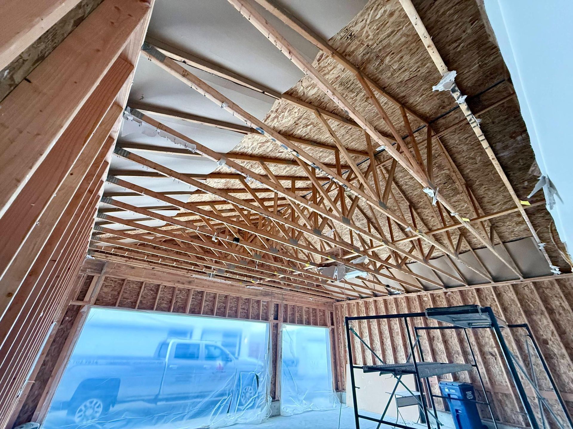 Interior view of a garage under construction with wooden framing and a truck visible through the opening.