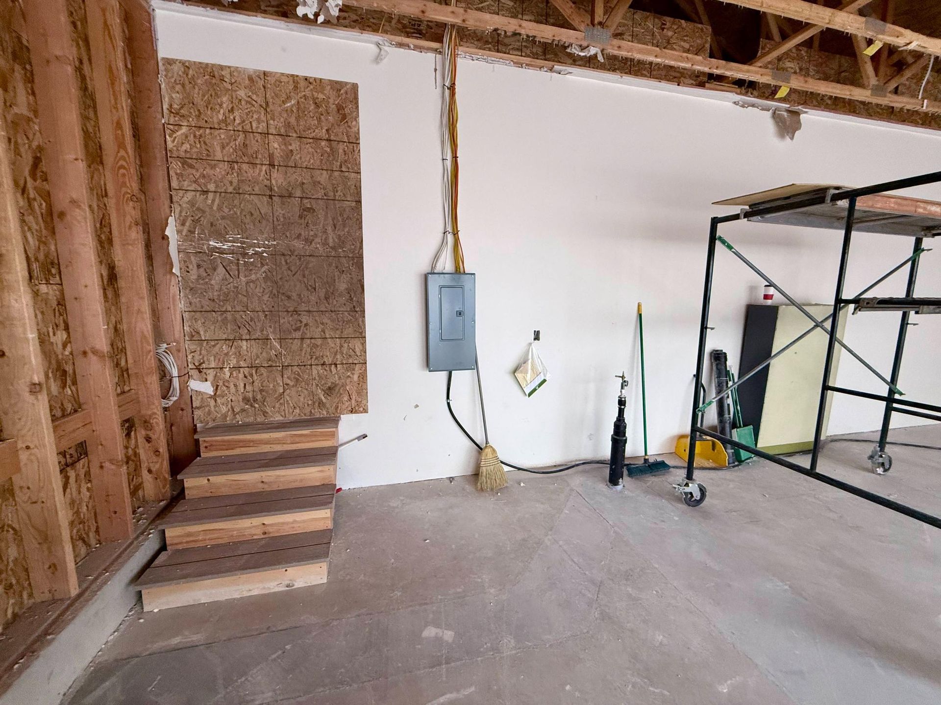 Construction site interior; wooden framing, concrete floor, electrical box, scaffolding, and drywall.