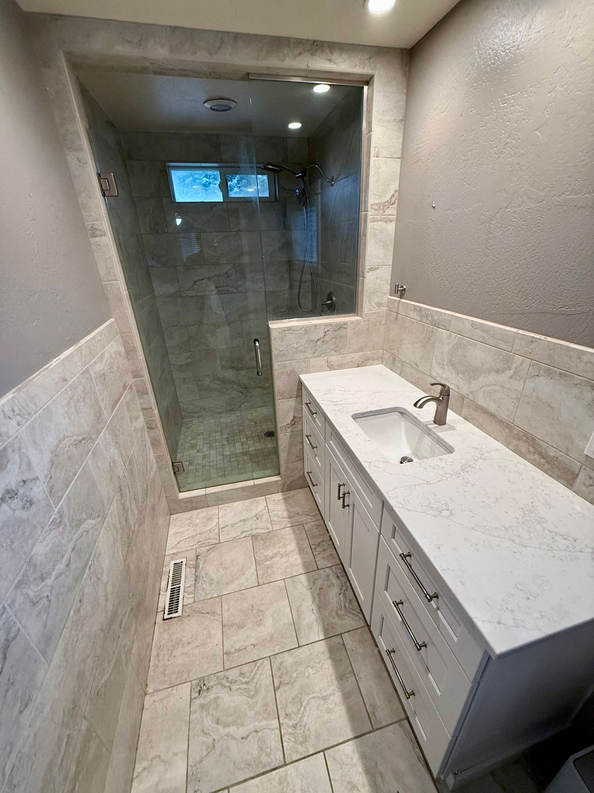 Bathroom with white vanity, walk-in shower with glass doors, and tiled walls and floor.