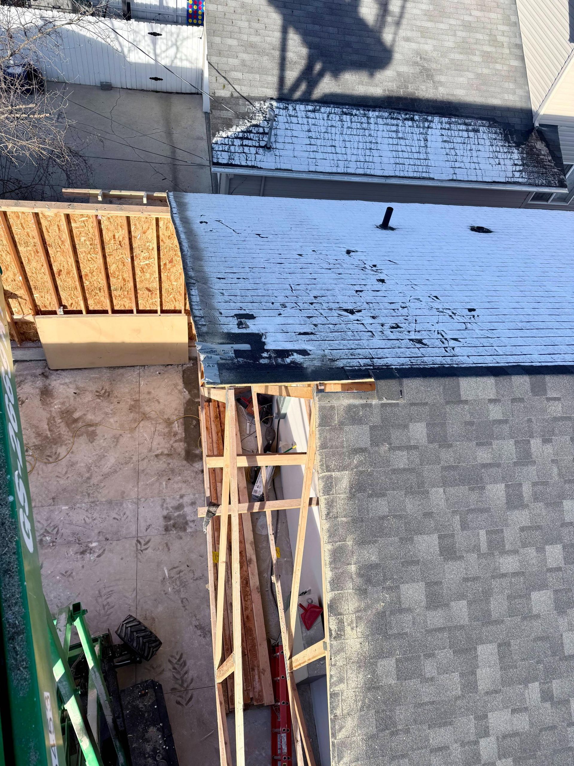 Overhead view of rooftops, with construction materials and scaffolding visible. Shadow of person on roof.