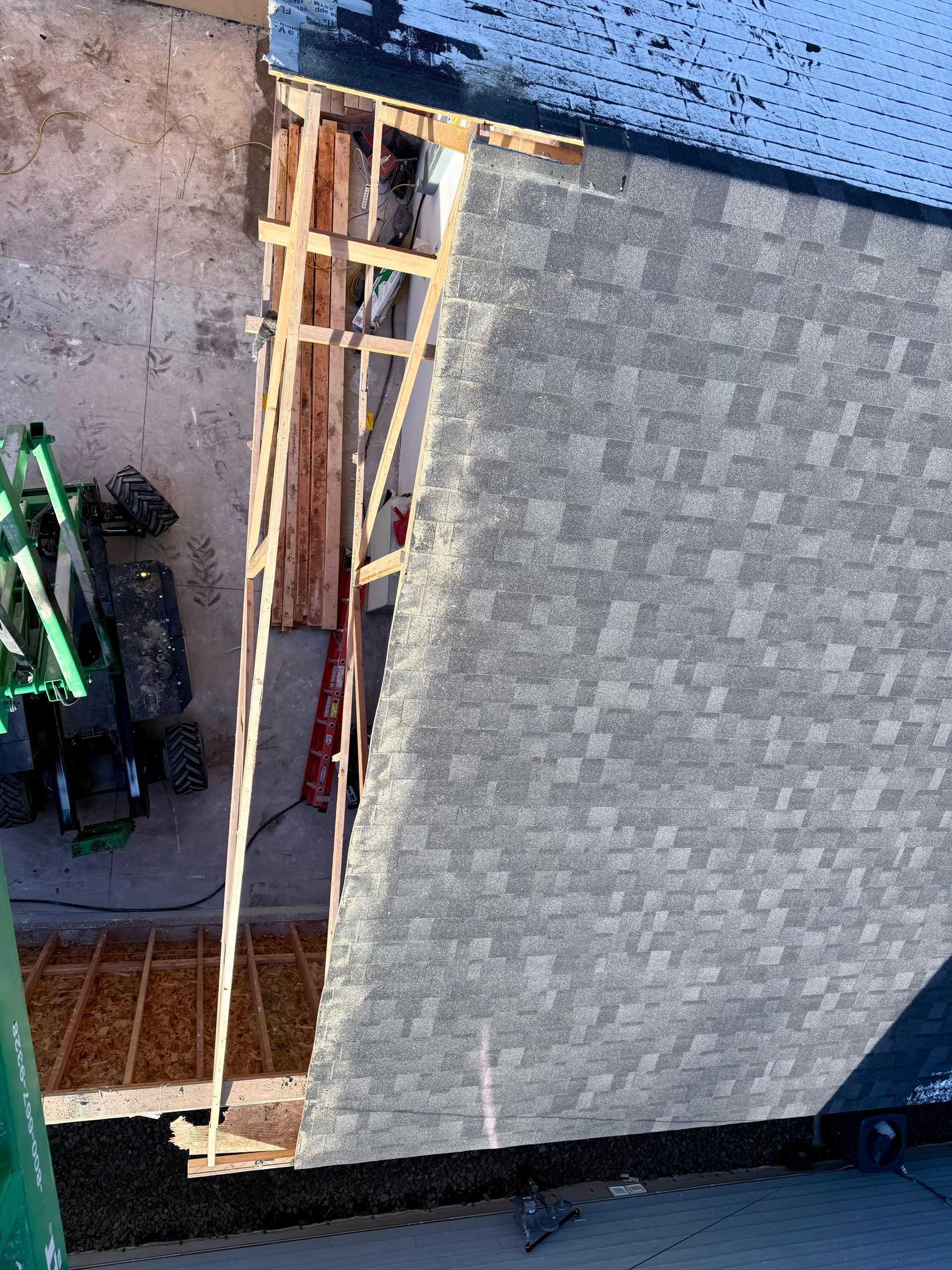 Construction scene: A roof with shingles, wooden frame, and machinery.