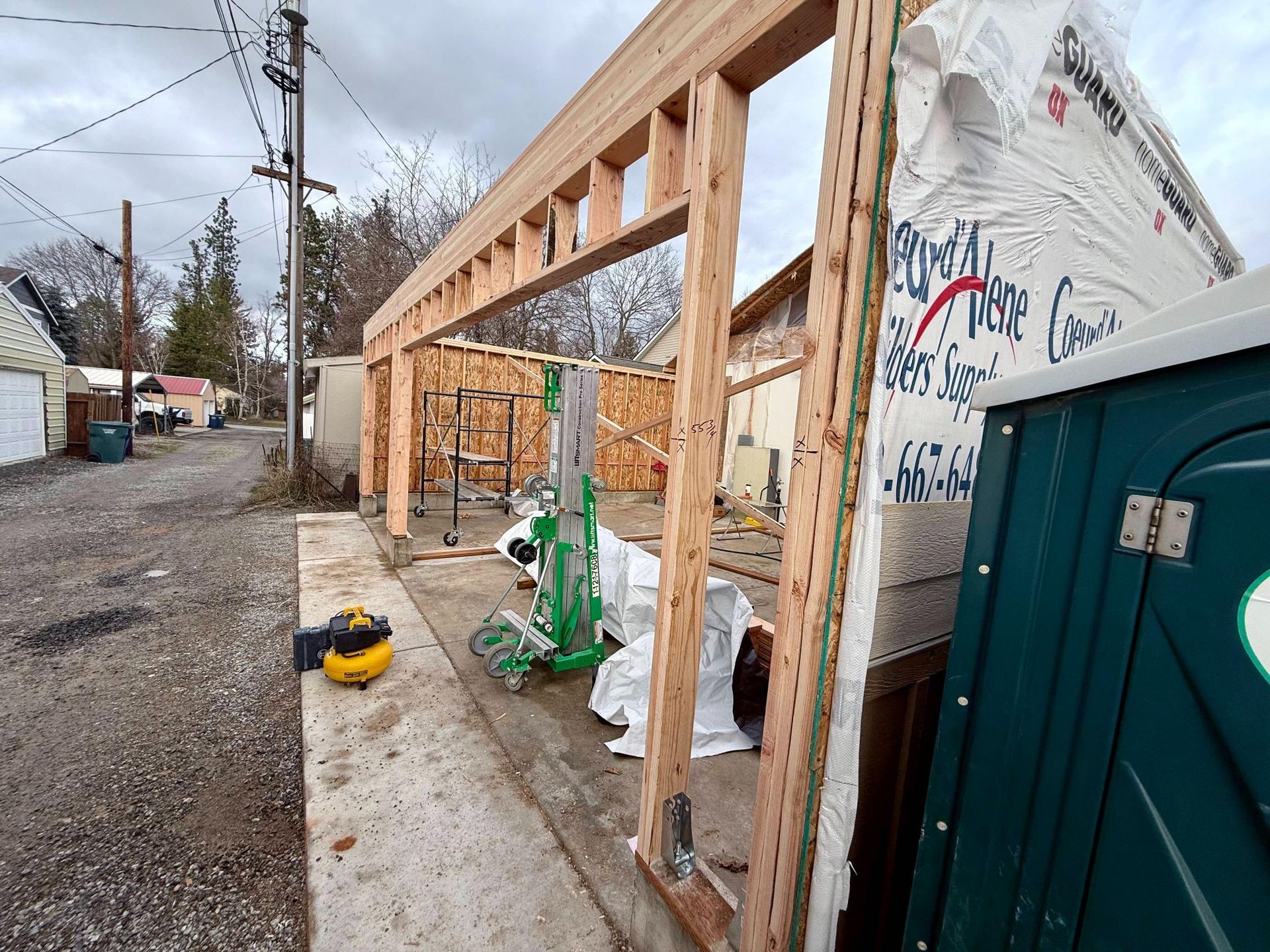 Construction of a wooden frame building next to a concrete structure; porta-potty on the right.
