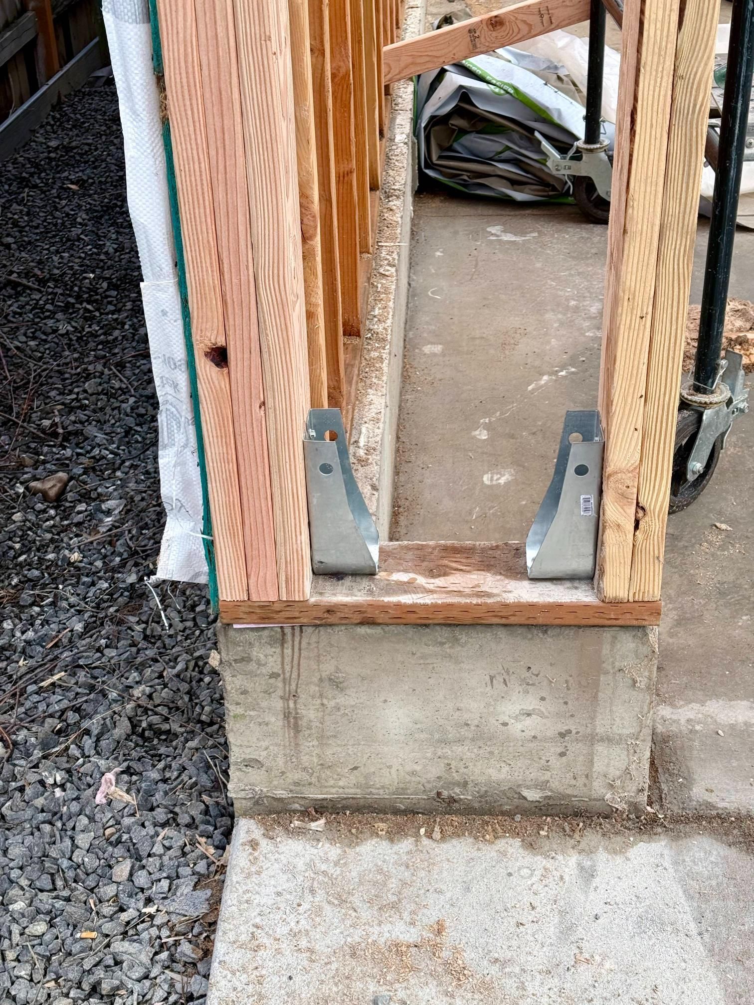 Framed wooden doorway with metal brackets on a concrete foundation, gravel on the left.