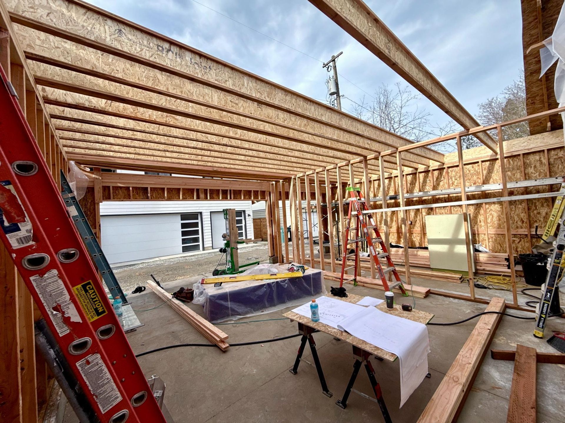 Construction site: wooden framework of a garage with visible beams and walls, open to the sky.