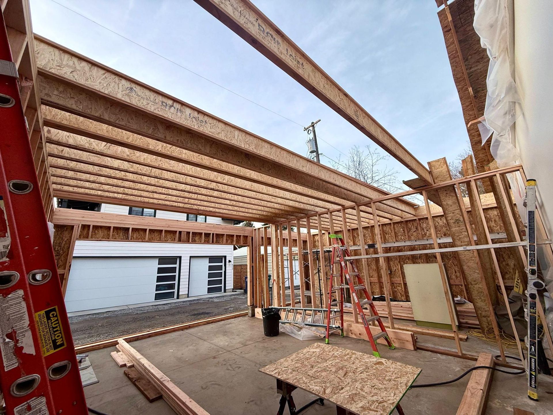 Construction site with wooden framing and steel beams for a building; a garage is visible in the background.