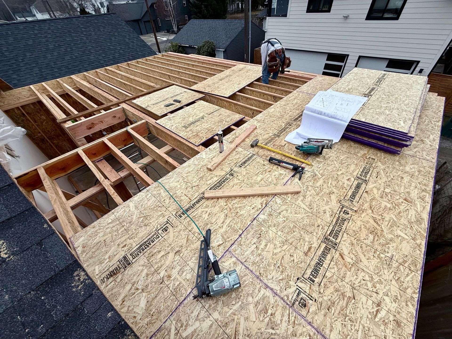 Construction workers installing plywood sheeting on a roof.