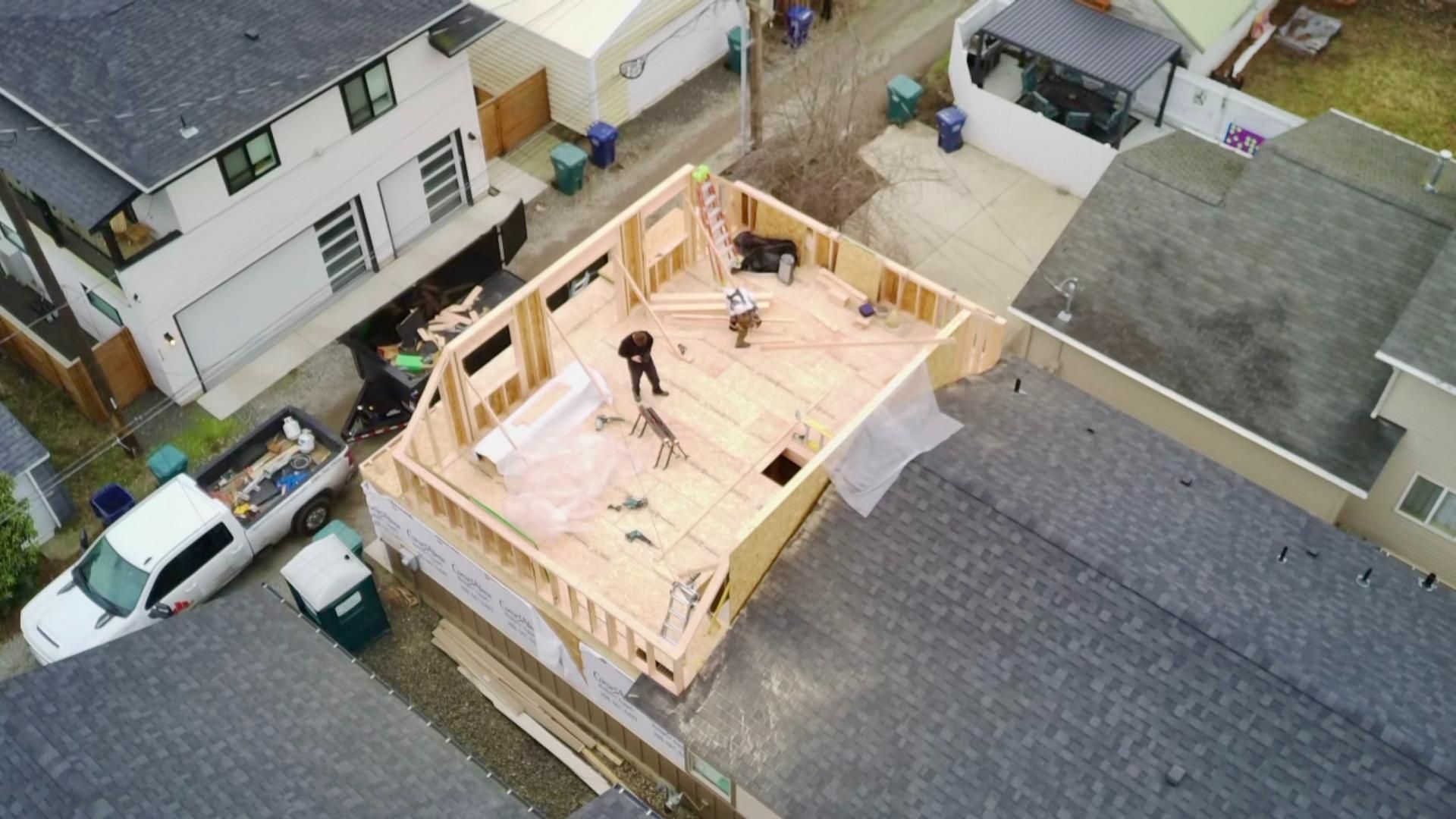 Aerial view of house construction with workers and a white truck. Wooden frame in progress.