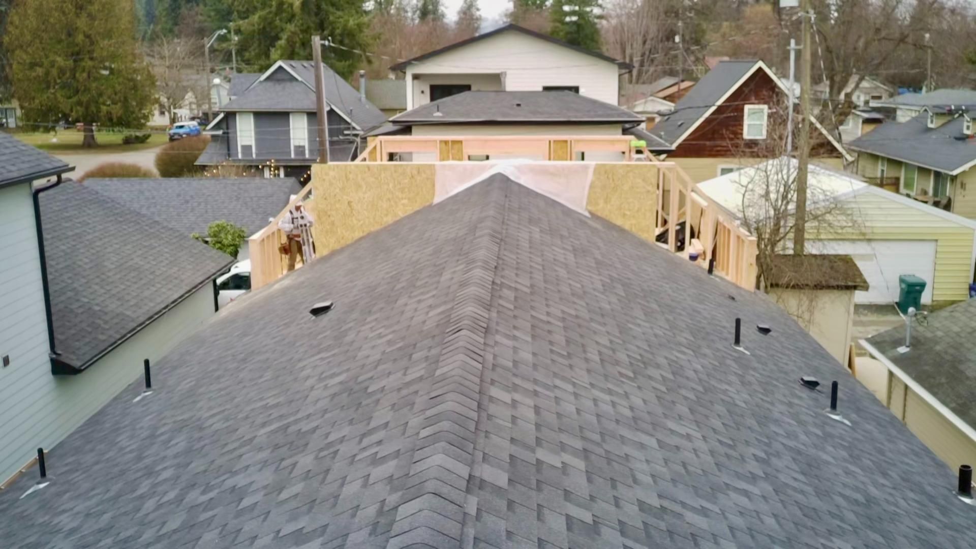View of grey shingled rooftops, homes in background, construction in progress.
