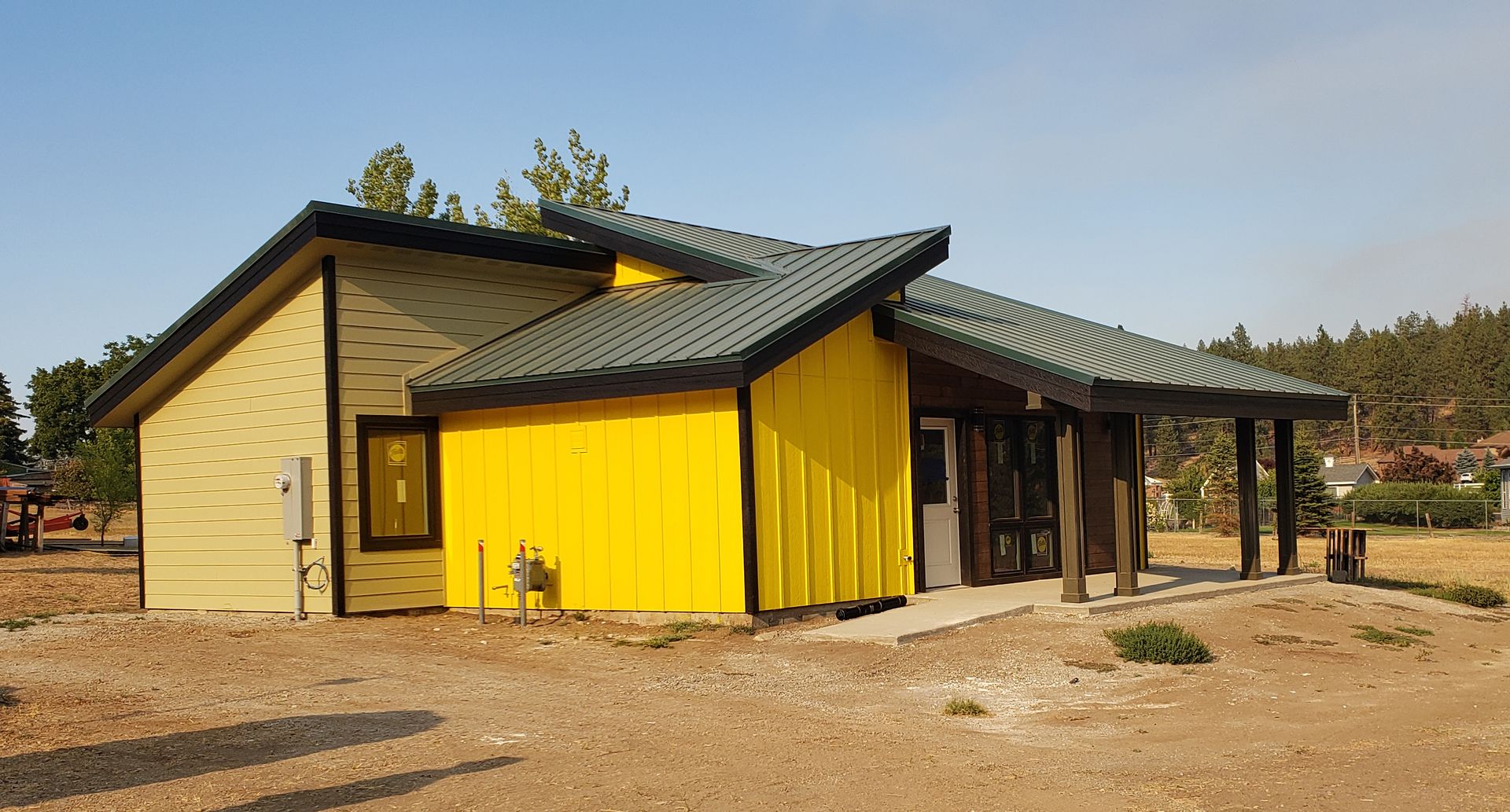 Yellow and tan building with a dark roof and porch, outdoors.