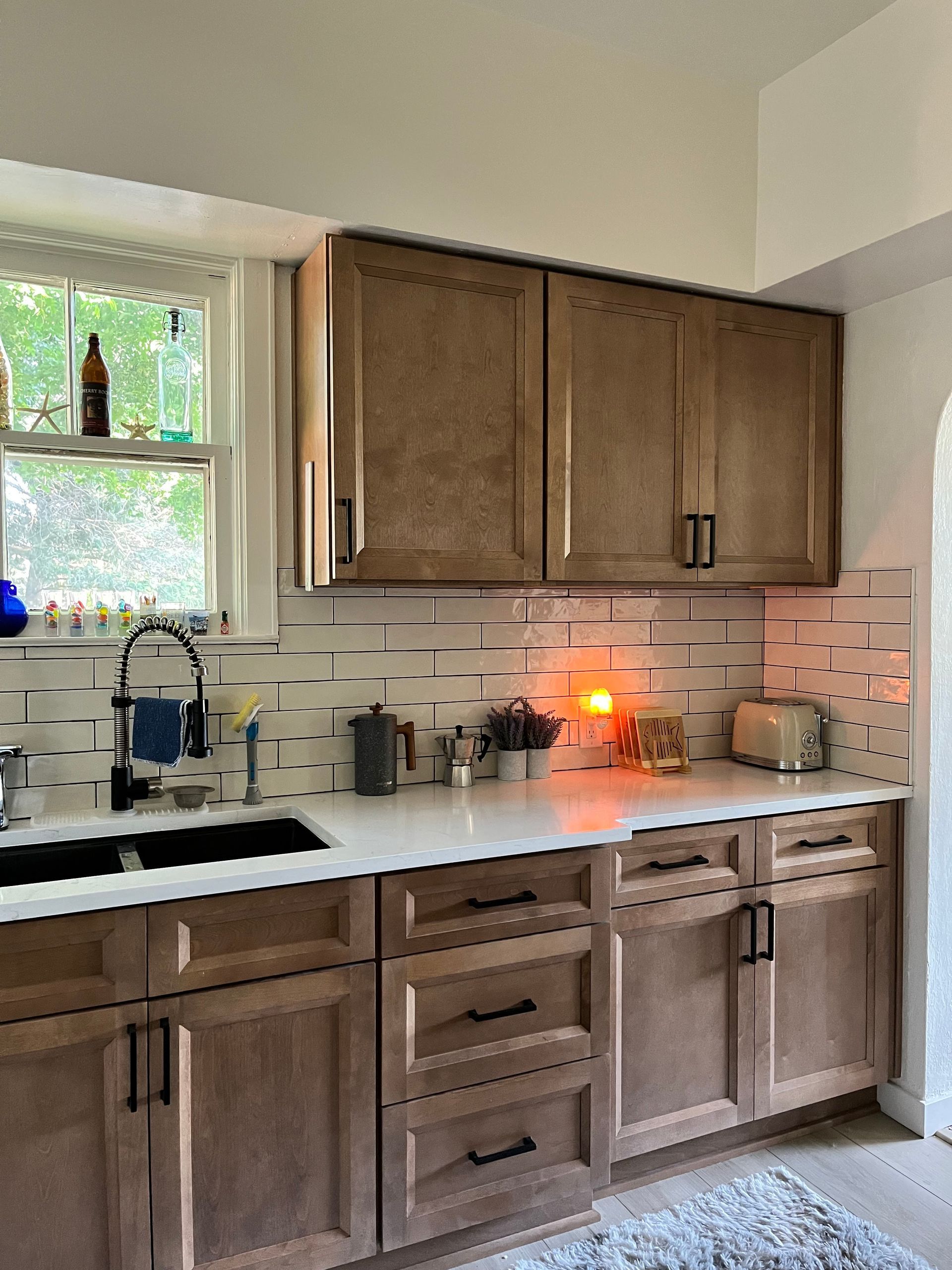 Kitchen with wooden cabinets, black hardware, white countertops, and a window with a view.