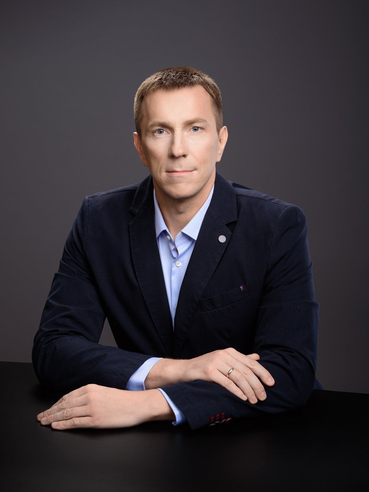A man in a suit is sitting at a table with his hands folded.