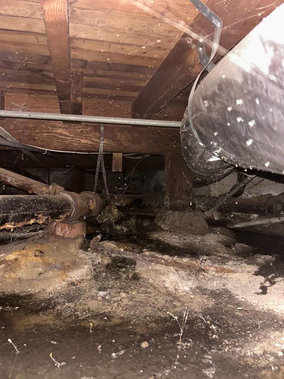 A dirty crawl space with a lot of pipes and wires in Huntington Beach.