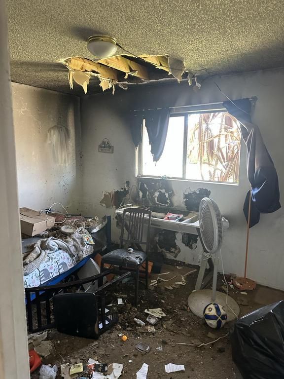 A messy room with a bed , desk , chair and fan.