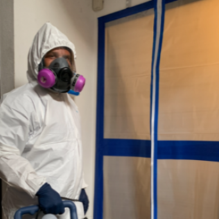 A man wearing a protective suit and mask is standing in a room.