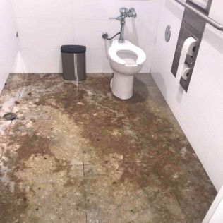 A toilet in a bathroom with a dirty floor in Huntington Beach.