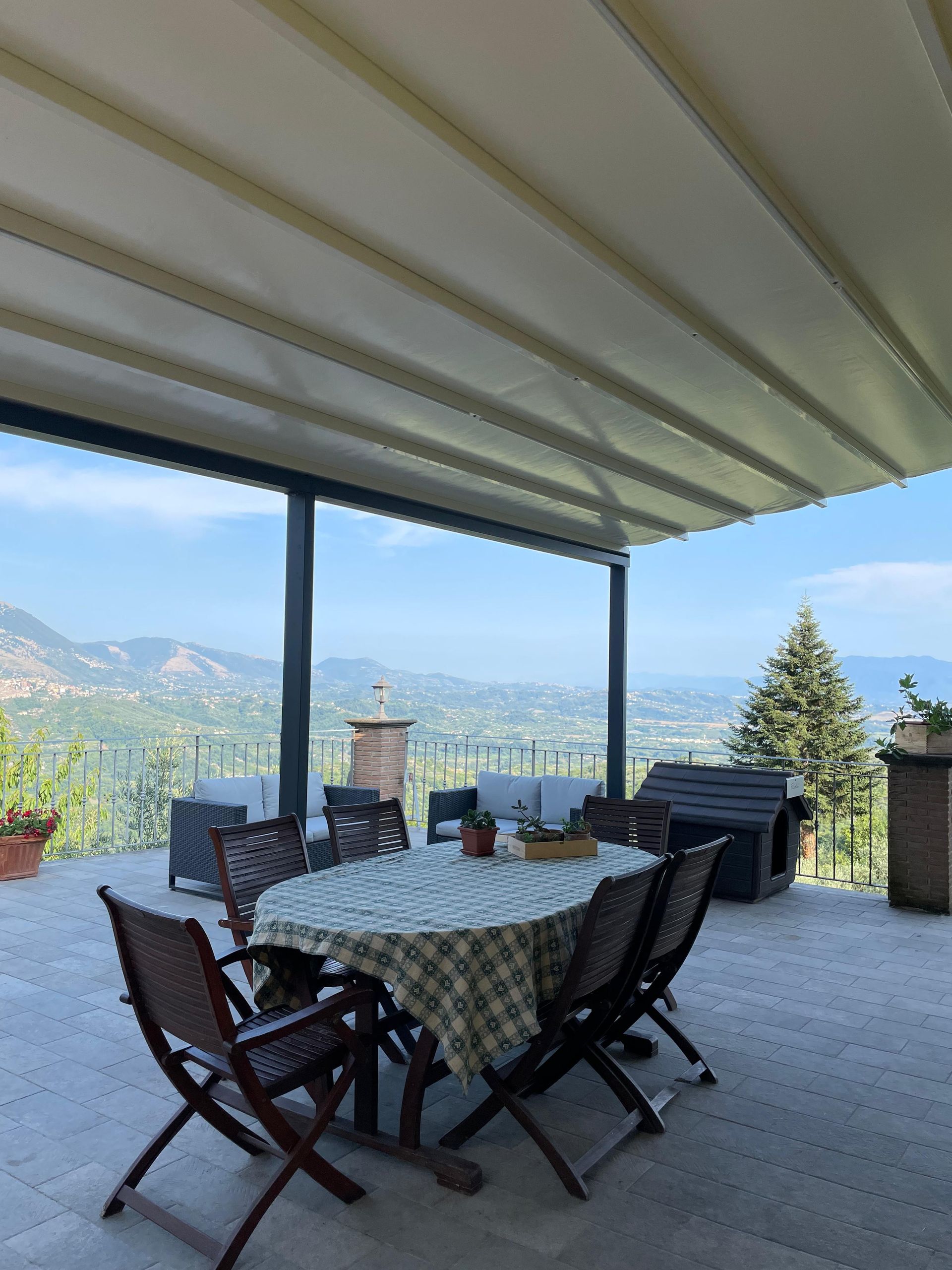 Patio con tavolo e sedie sotto una tenda da sole retrattile, con vista su un paesaggio in lontananza.