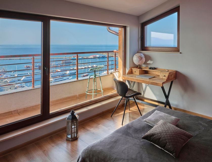 Camera da letto con scrivania, letto e balcone con vista sul porto e sul mare blu.