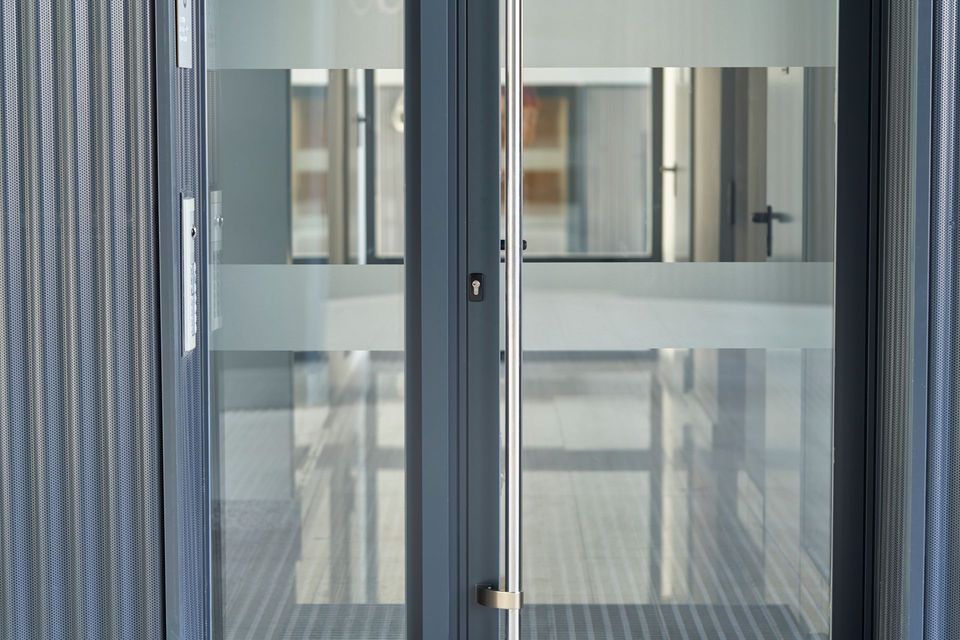Doppie porte in vetro con fasce orizzontali smerigliate, che riflettono un corridoio interno.